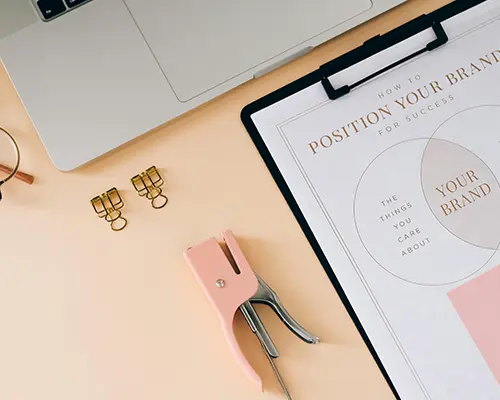 Flat lay of branding materials including a clipboard with brand strategy, laptop, and office supplies.