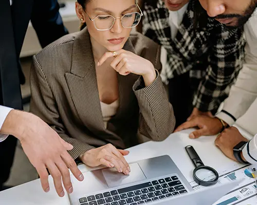 Group of professionals collaborating around a laptop in a modern office setting.