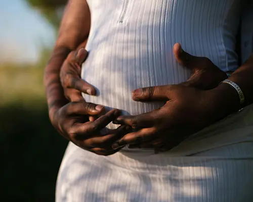 Hands gently resting on a pregnant woman’s belly, captured in natural light.
