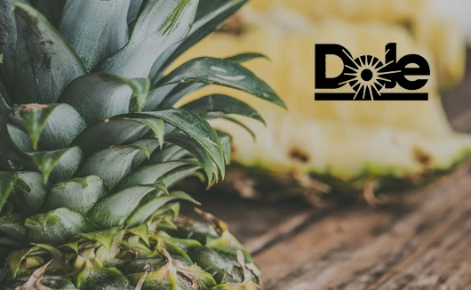 Close-up of a fresh pineapple with sliced fruit in the background, Dole logo top right.