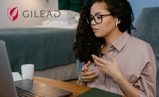 Woman wearing glasses and earbuds speaking during a video call, with Gilead logo in the background.