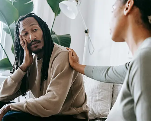 Woman gently comforting a man with her hand on his shoulder during a serious conversation.