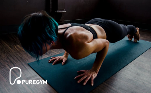 Woman with short hair doing a plank or push-up on a yoga mat at a gym.