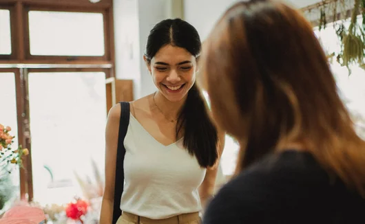 Young woman smiling as she chats with another person inside a boutique-style shop.