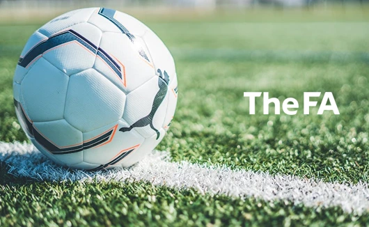 Close-up of a Puma football resting on a white line on a grassy football pitch, with The FA logo.