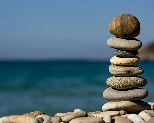 Stack of balanced pebbles on a rocky beach with a calm ocean in the background.