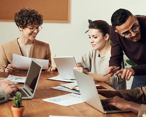 Group of professionals in a team meeting, collaborating around a table with laptops and documents.