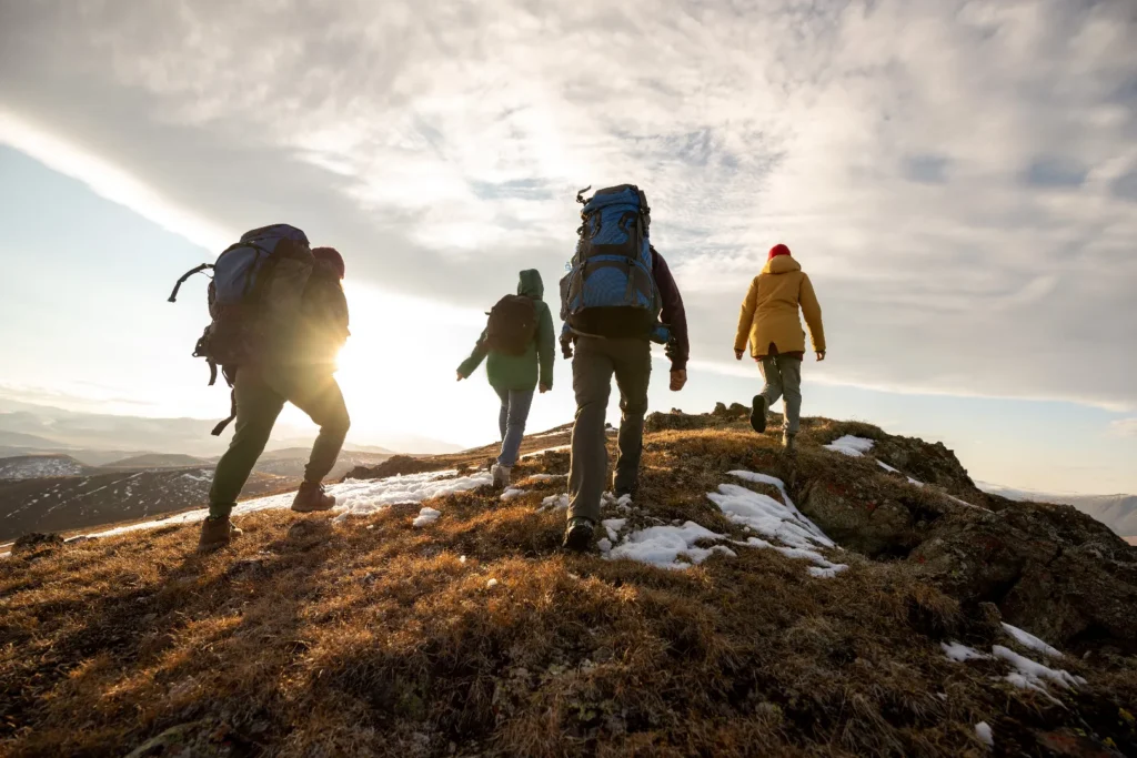 A group of hikers walking up a snowy hill as the sun sets